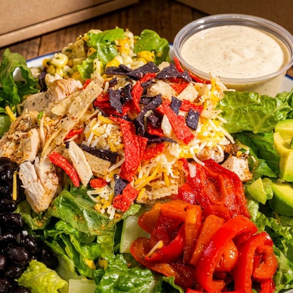 Vibrant chicken salad with black beans, avocado, roasted peppers, and tortilla strips on a wooden table.